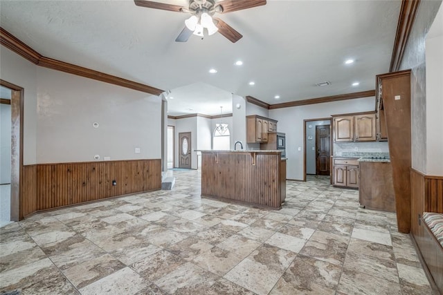 kitchen featuring kitchen peninsula, ornamental molding, ceiling fan, wooden walls, and sink