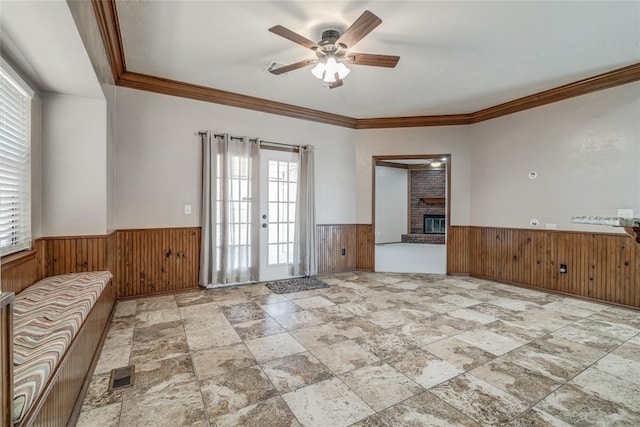 empty room with ceiling fan, french doors, wood walls, a fireplace, and ornamental molding