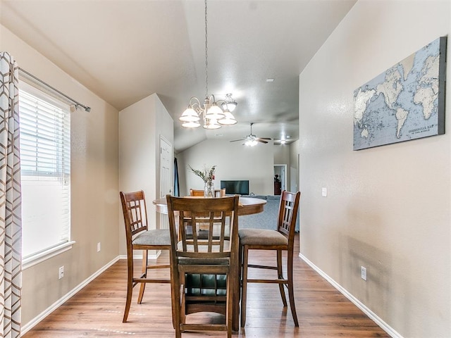 dining space featuring ceiling fan with notable chandelier, hardwood / wood-style flooring, and vaulted ceiling