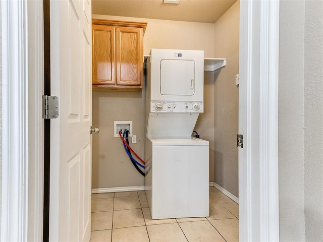 clothes washing area featuring cabinets, stacked washer / drying machine, and light tile patterned flooring