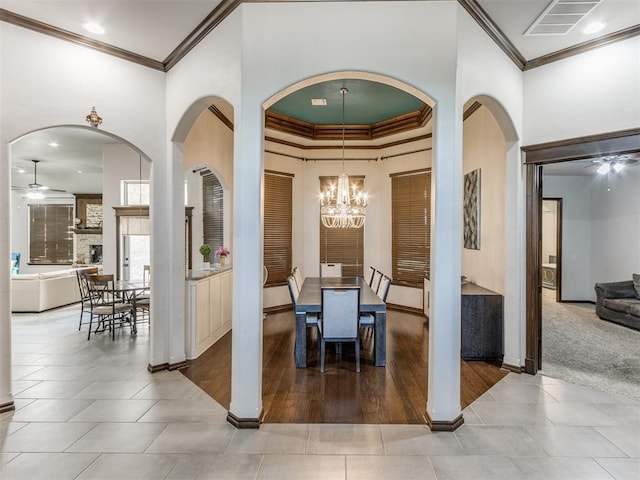 dining room with ceiling fan with notable chandelier, light hardwood / wood-style floors, ornamental molding, and a fireplace