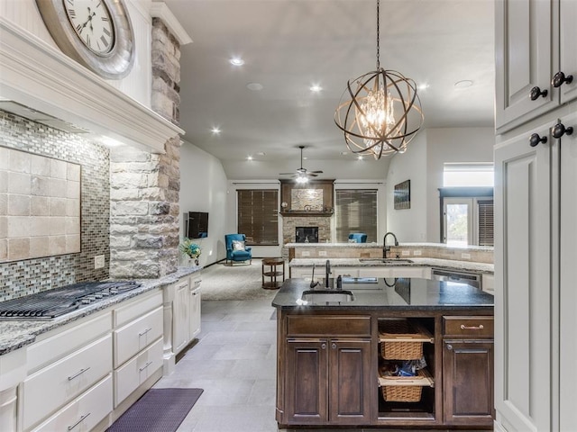 kitchen with dark brown cabinetry, a kitchen island with sink, sink, a fireplace, and stainless steel gas stovetop