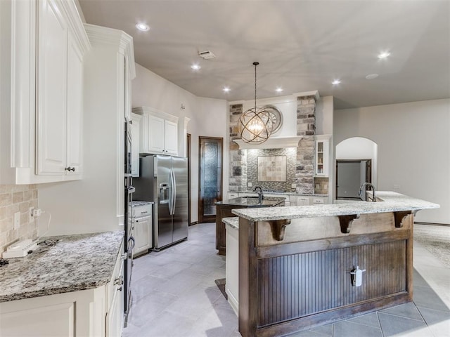 kitchen featuring pendant lighting, a breakfast bar, white cabinets, stainless steel refrigerator with ice dispenser, and a large island