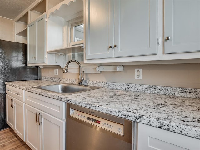 kitchen with light stone countertops, light wood-type flooring, stainless steel dishwasher, sink, and white cabinets