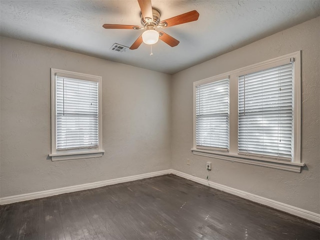 empty room with a wealth of natural light, ceiling fan, and dark wood-type flooring