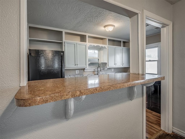 kitchen with black refrigerator, a kitchen bar, sink, hardwood / wood-style flooring, and white cabinetry