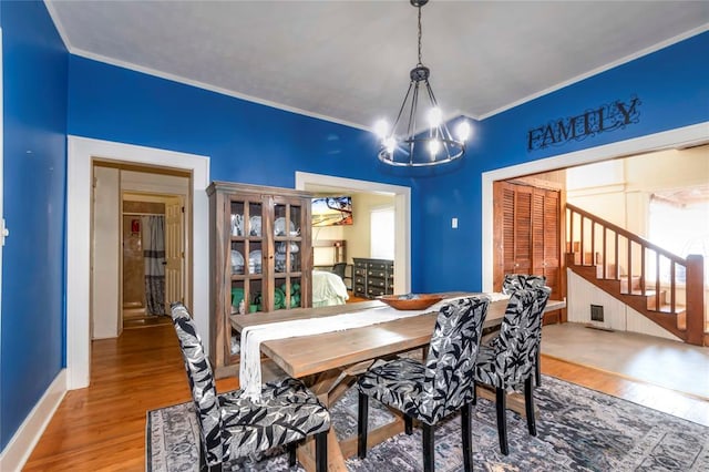 dining area with wood-type flooring, ornamental molding, and an inviting chandelier