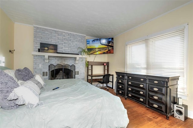 bedroom with hardwood / wood-style floors, ornamental molding, and a fireplace