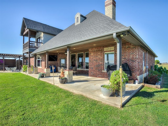 rear view of house with ceiling fan, a patio area, a balcony, and a lawn