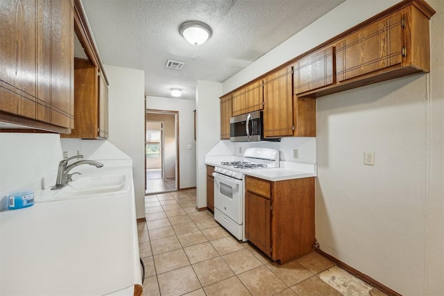 kitchen featuring sink, light tile patterned floors, white range with gas stovetop, and a textured ceiling