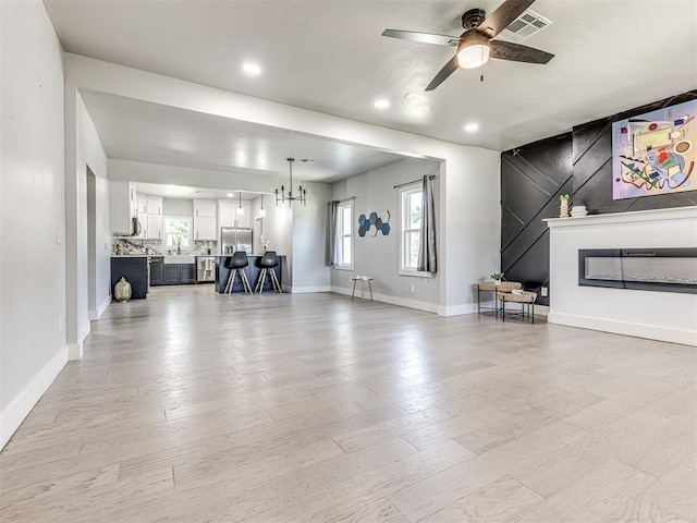 unfurnished living room with ceiling fan with notable chandelier and light wood-type flooring