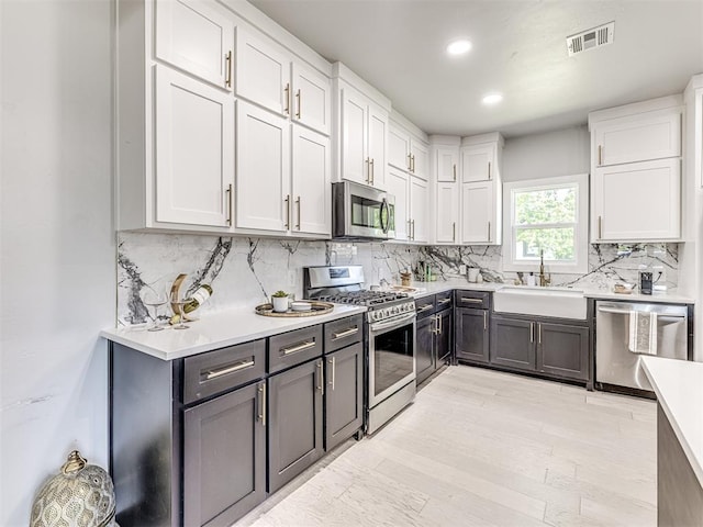 kitchen with white cabinets, sink, light hardwood / wood-style flooring, decorative backsplash, and appliances with stainless steel finishes