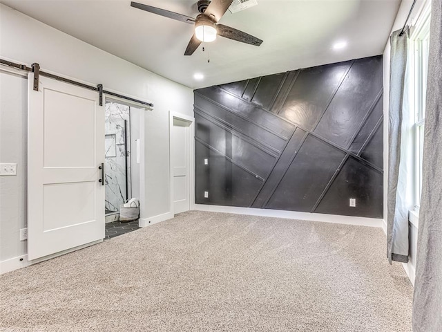 unfurnished room featuring a barn door, carpet floors, and ceiling fan