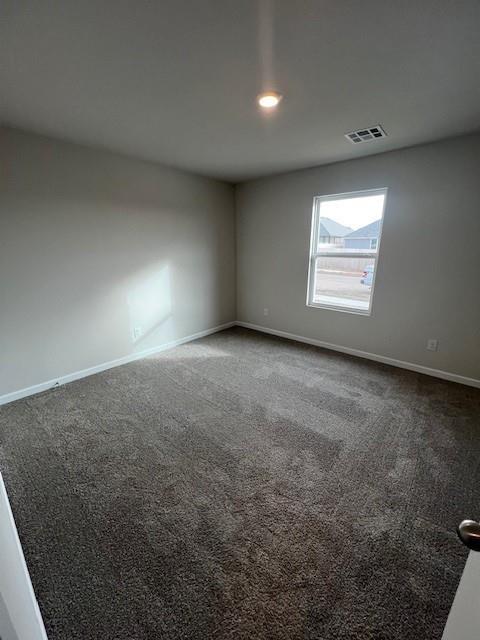 unfurnished room with visible vents, baseboards, and dark carpet