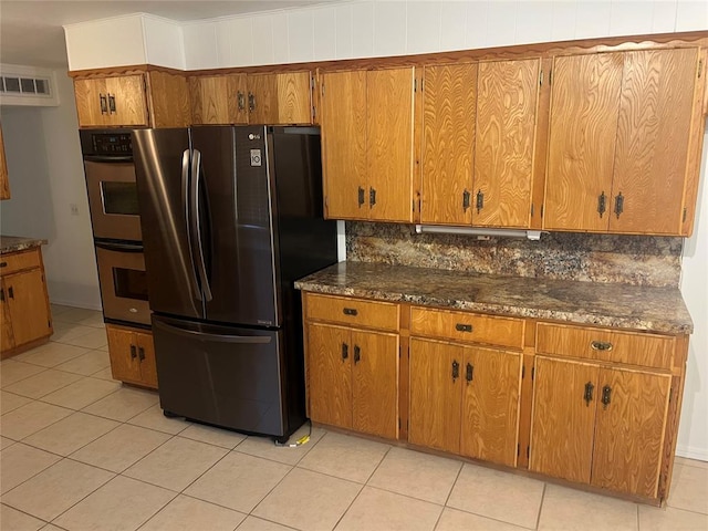 kitchen with backsplash, light tile patterned flooring, stainless steel appliances, and dark stone counters