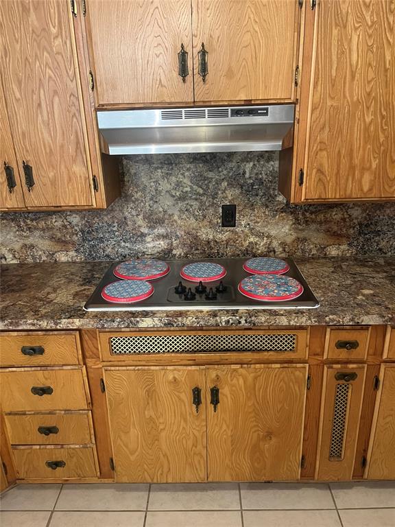 kitchen featuring backsplash, dark stone countertops, extractor fan, black electric stovetop, and light tile patterned floors