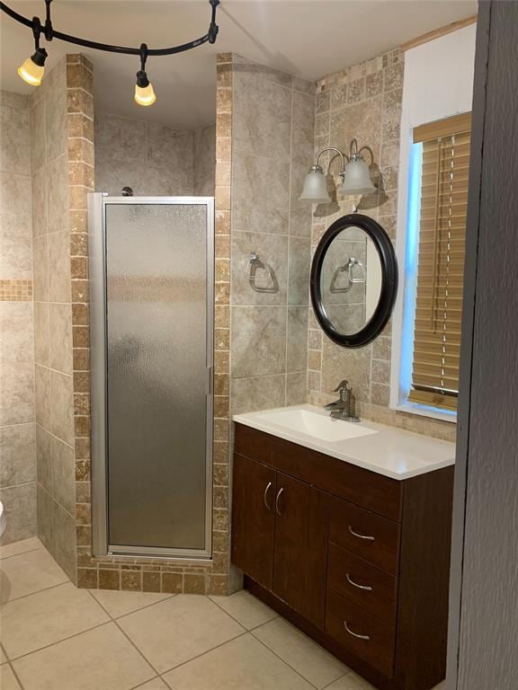 bathroom featuring tile patterned floors, vanity, a shower with shower door, and tile walls