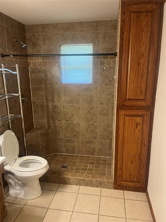 bathroom with tile patterned flooring, vanity, tiled shower, and toilet