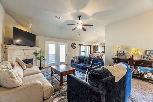 carpeted living room with a tiled fireplace, ceiling fan with notable chandelier, and vaulted ceiling