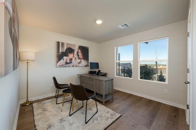 office space with baseboards, visible vents, and wood finished floors