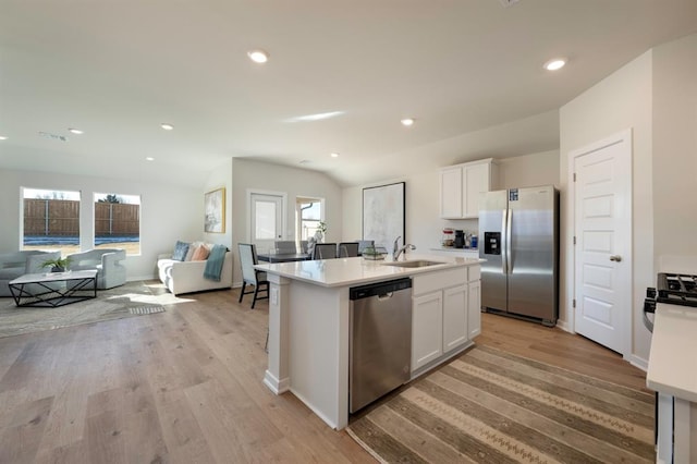 kitchen featuring an island with sink, open floor plan, stainless steel appliances, light countertops, and white cabinetry