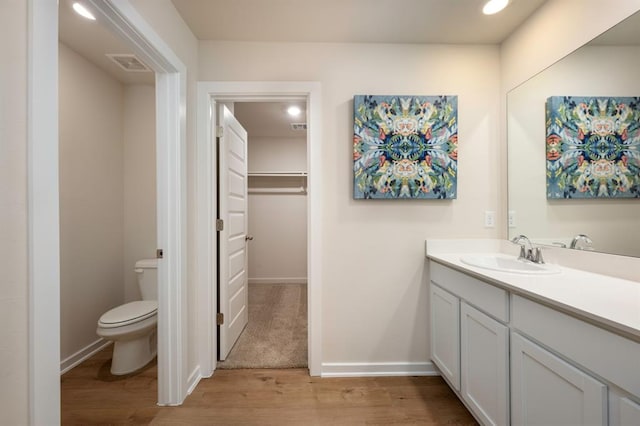 bathroom featuring visible vents, toilet, wood finished floors, a walk in closet, and vanity