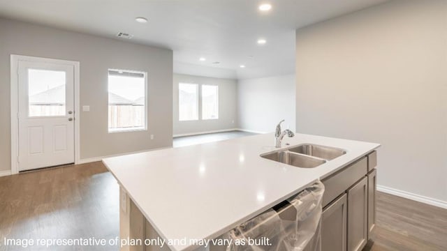 kitchen featuring a center island with sink, visible vents, wood finished floors, light countertops, and a sink