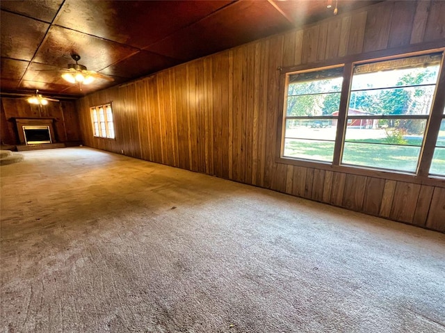 unfurnished living room with ceiling fan, wood walls, and carpet floors