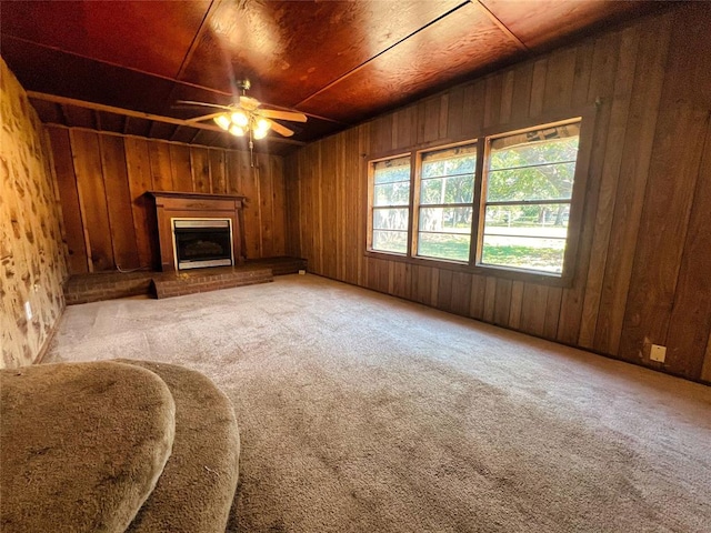 unfurnished living room with carpet flooring, ceiling fan, wooden ceiling, a brick fireplace, and wood walls