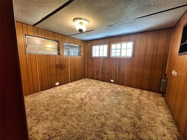 empty room with a textured ceiling, carpet floors, radiator, and wood walls