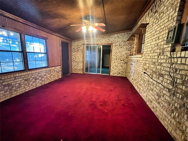 carpeted spare room featuring ceiling fan, ornamental molding, and brick wall