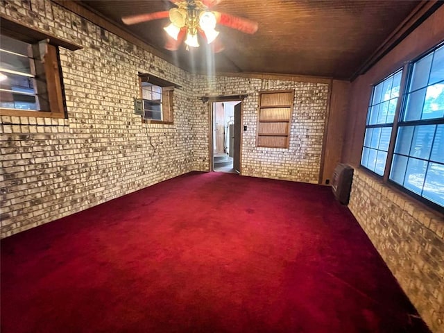 carpeted spare room with lofted ceiling, crown molding, ceiling fan, radiator heating unit, and brick wall