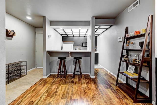 kitchen featuring kitchen peninsula, a kitchen bar, hardwood / wood-style flooring, and white fridge