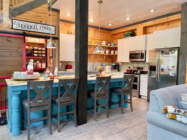 kitchen featuring a kitchen breakfast bar, wood walls, pendant lighting, appliances with stainless steel finishes, and light wood-type flooring