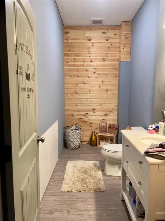 bathroom with hardwood / wood-style floors, vanity, toilet, and wood walls