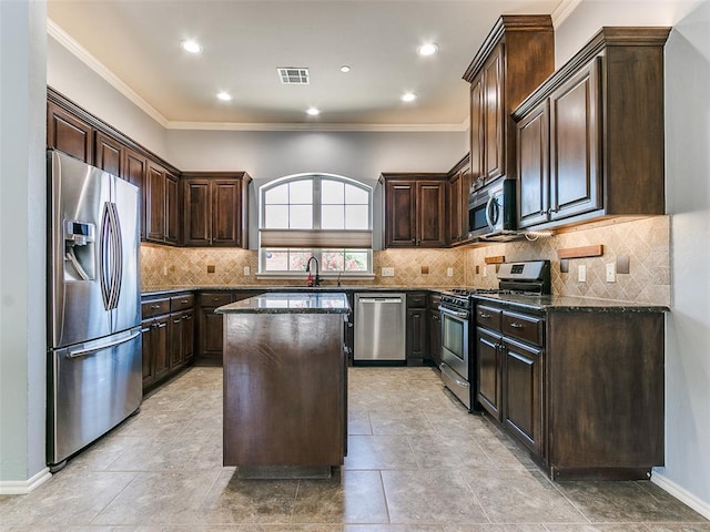 kitchen featuring dark brown cabinetry, appliances with stainless steel finishes, a kitchen island, dark stone counters, and sink