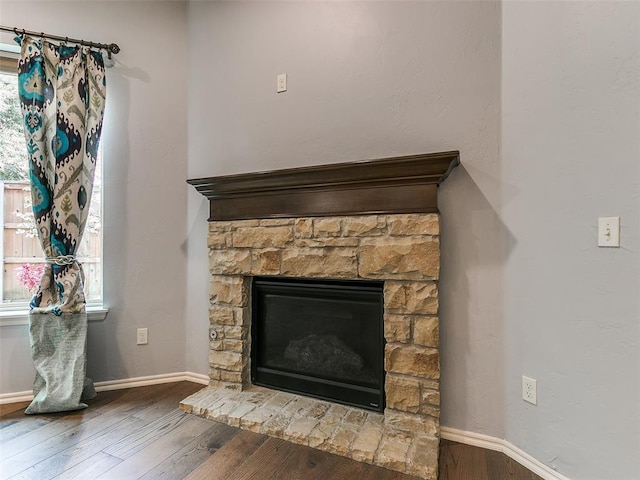 details with baseboards, wood finished floors, and a stone fireplace