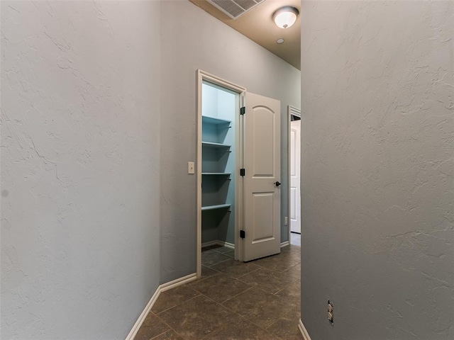 hallway with a textured wall, dark tile patterned flooring, visible vents, and baseboards