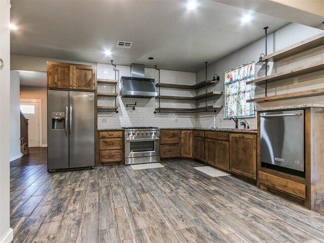 kitchen featuring dark wood-type flooring, stainless steel appliances, wall chimney range hood, and sink