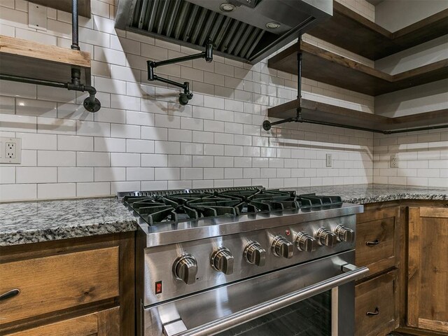 kitchen featuring stone countertops, high end stove, range hood, and tasteful backsplash