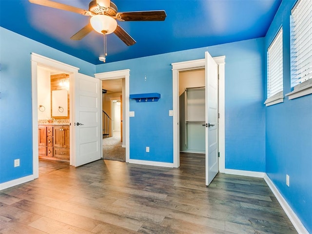 unfurnished bedroom with ceiling fan, sink, wood-type flooring, a spacious closet, and a closet