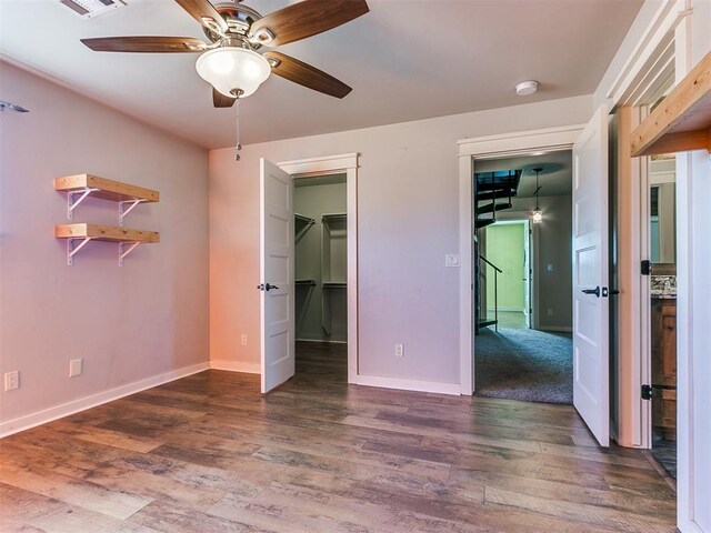 unfurnished bedroom with a spacious closet, a closet, dark wood-type flooring, and ceiling fan