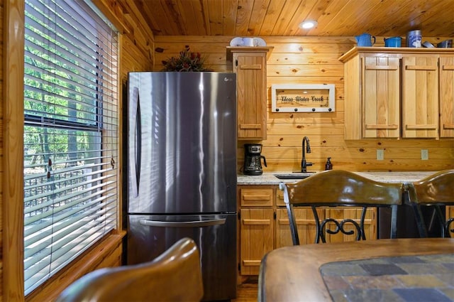 kitchen featuring light stone countertops, sink, wooden ceiling, stainless steel fridge, and wood walls