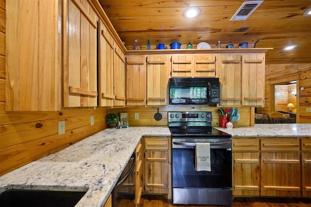 kitchen featuring black appliances, dark hardwood / wood-style floors, light stone counters, and wooden walls