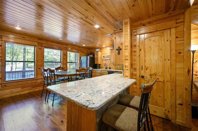 kitchen with wood walls, light stone countertops, dark hardwood / wood-style flooring, kitchen peninsula, and stainless steel refrigerator