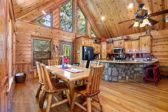 dining space with wooden walls, light wood-type flooring, and high vaulted ceiling