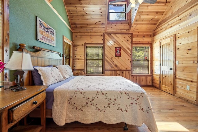 bedroom with wooden ceiling, light hardwood / wood-style floors, lofted ceiling with skylight, and wooden walls