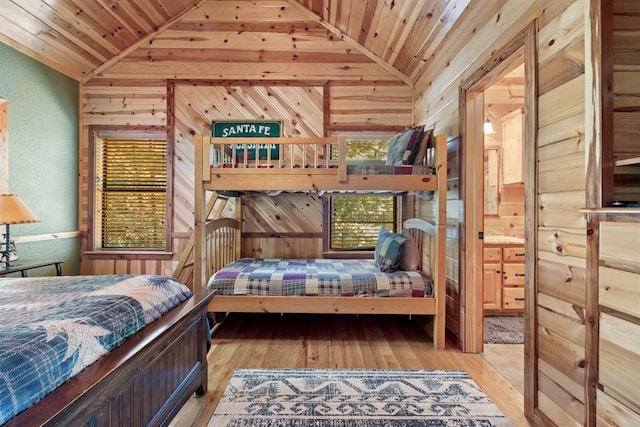 bedroom featuring ensuite bathroom, light hardwood / wood-style flooring, wood walls, and lofted ceiling