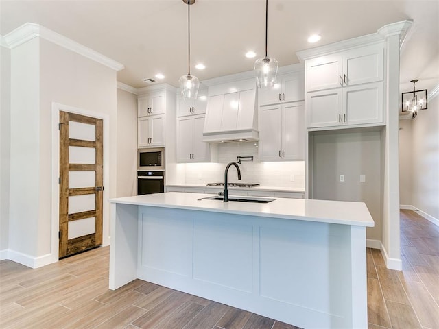 kitchen featuring white cabinetry, a center island with sink, decorative light fixtures, and custom exhaust hood