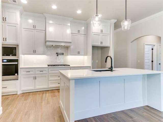 kitchen with light hardwood / wood-style flooring, decorative light fixtures, a kitchen island with sink, white cabinets, and appliances with stainless steel finishes